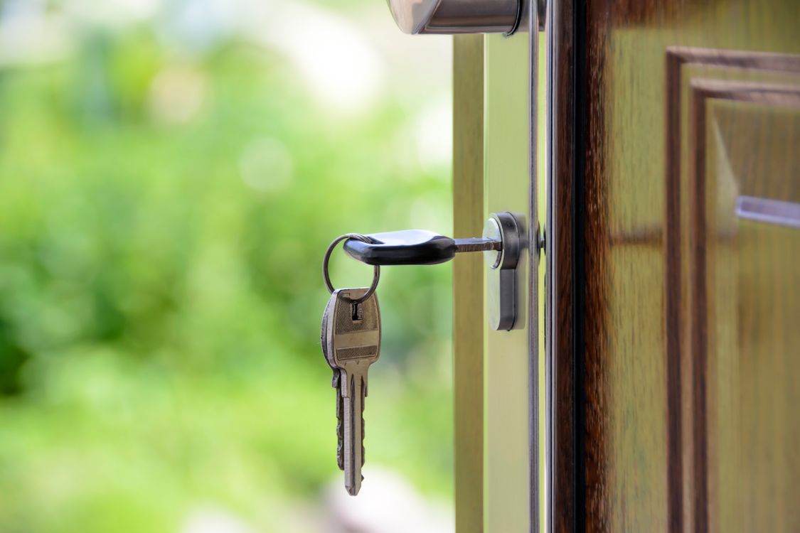 A smiling couple holds up keys in a bright, empty room, celebrating the financial savings and reduced stress of selling their home.